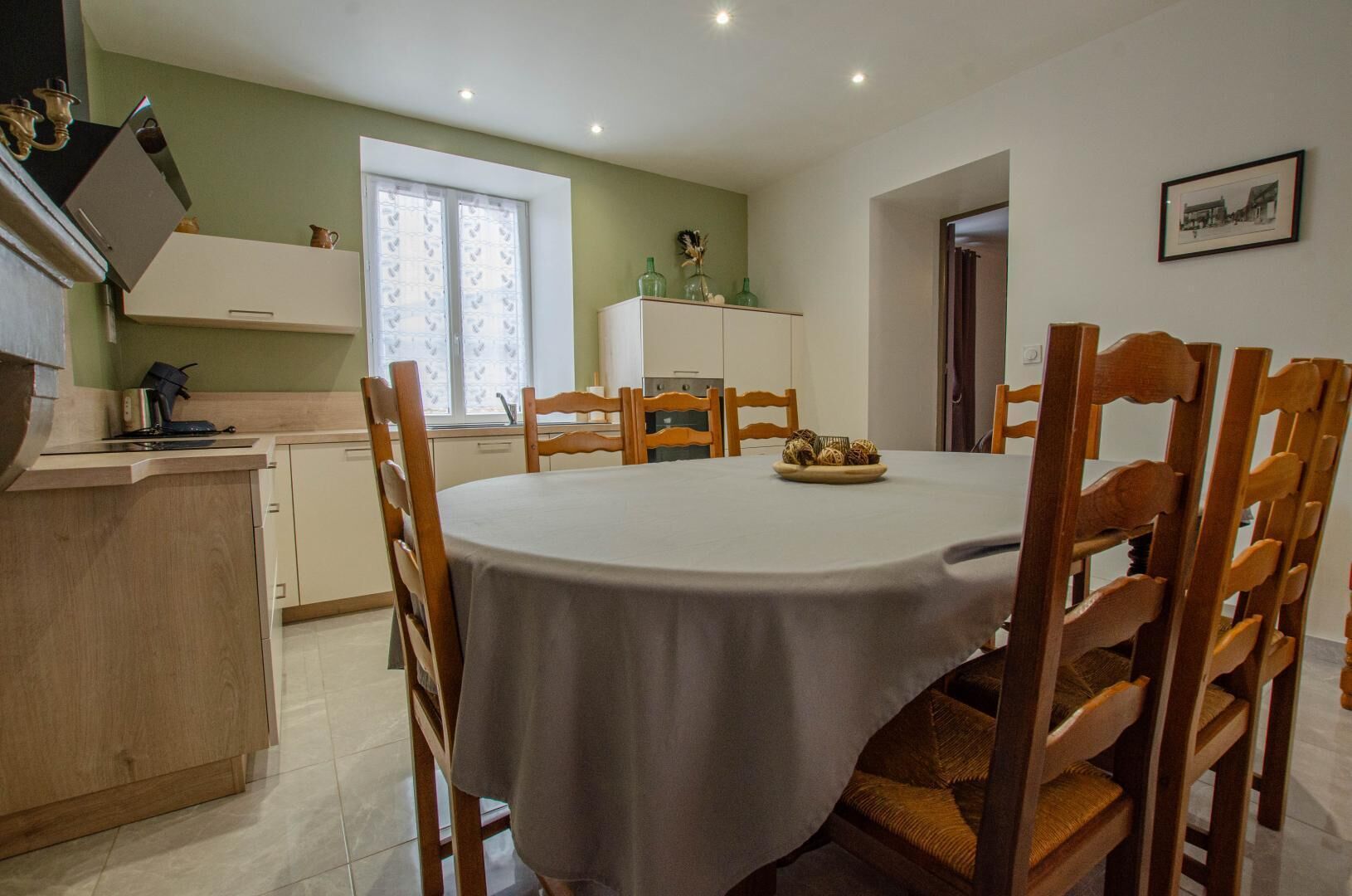 A dining area with a round table, wooden chairs, and a white tablecloth.