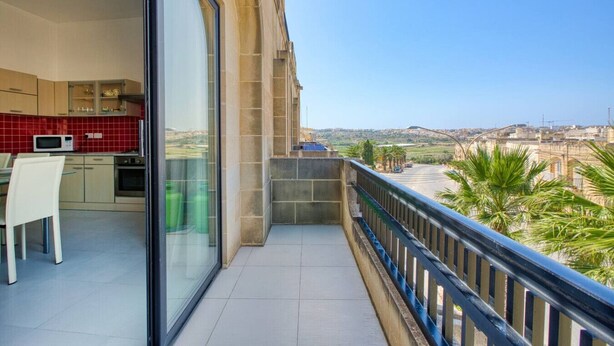 Ein Balkon mit Blick auf eine Stadtlandschaft, eine Küche mit roten Fliesen und eine Essecke mit einem weißen Stuhl.