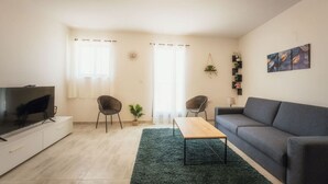 Ein modernes Wohnzimmer mit Flachbildfernseher, zwei Sessel, einer Couch, einem Couchtisch und einer Topfpflanze.