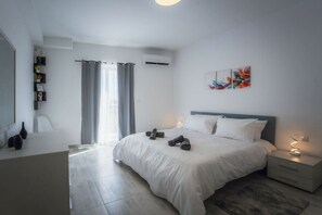 A modern bedroom with a large bed, bedside tables, a desk, and a chair. - Gozo Haven Stylish Escape This Spacious 3-bed (Xewkija)