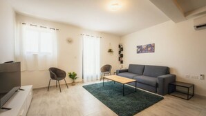 Ein modernes Wohnzimmer mit einem grauen Sofa, zwei Sesseln, einem Couchtisch und einem Fernseher auf einem Schrank.