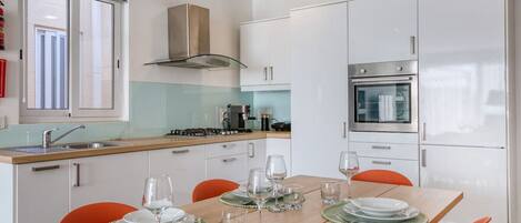 Une cuisine moderne avec des meubles blancs, un four en acier inoxydable et une cuisinière à gaz. On y trouve une table à manger mise avec des assiettes, des verres et des couverts.