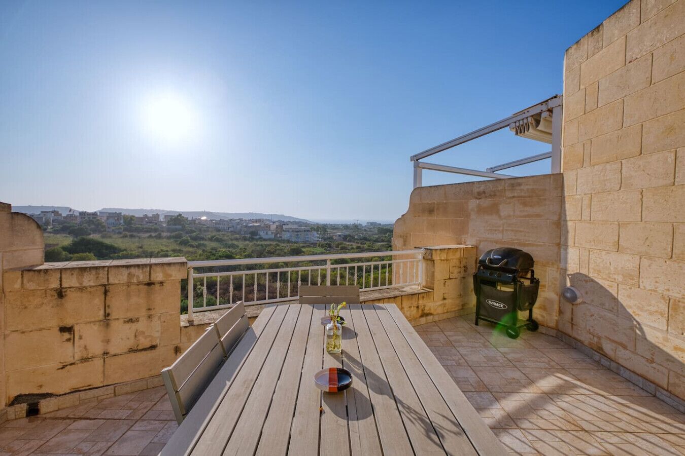 A wooden deck with a barbecue grill and a table with a bottle and glass.