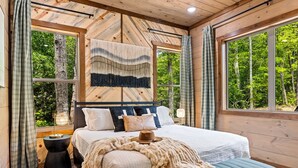 A bedroom with a large bed, wooden walls, and a view of trees.