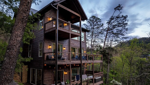 A multi-level wooden cabin with balconies, large windows, and outdoor seating areas.