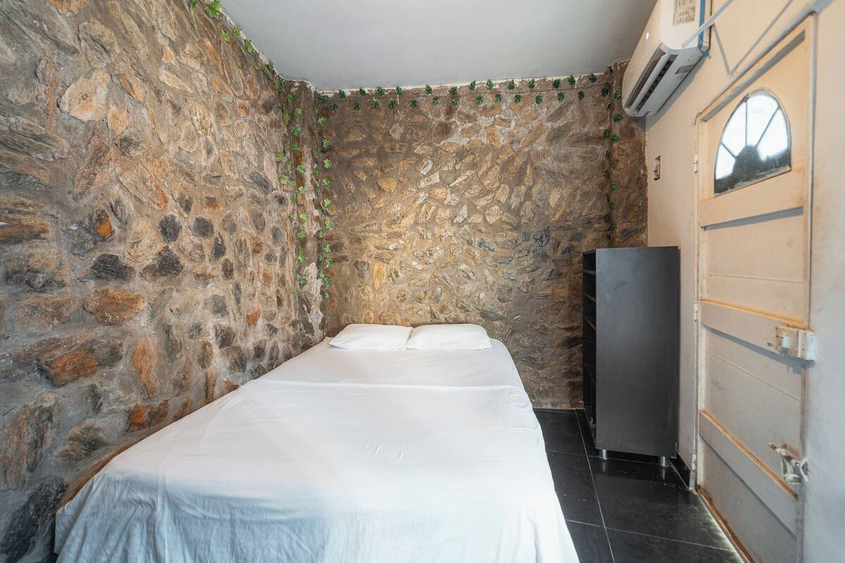 Una habitación con pared de piedra, una cama, un armario y un equipo de aire acondicionado.