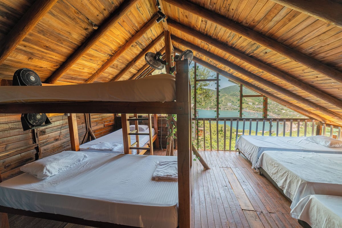 Una cabaña de madera con dos literas, un balcón con barandilla y vista a un lago y montañas.