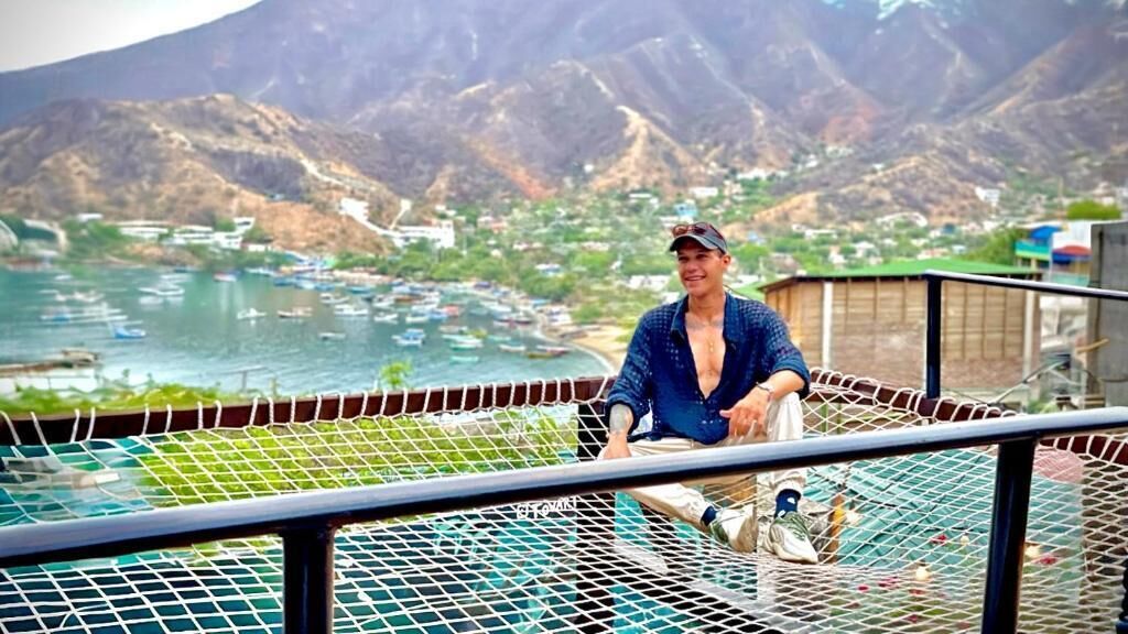 A person sitting on a balcony overlooking a mountainous landscape with a body of water and boats.