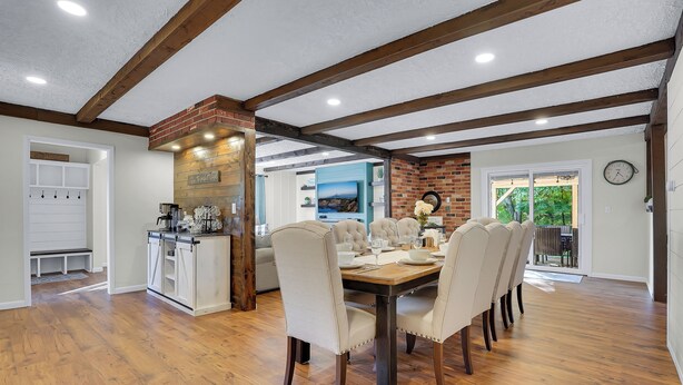 Un vaste espace dédié à la salle à manger, avec une table et des chaises en bois, un mur décoratif en briques et une vue sur l’extérieur.