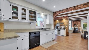 Une cuisine moderne avec des meubles blancs, un lave-vaisselle et un mur décoratif en briques.