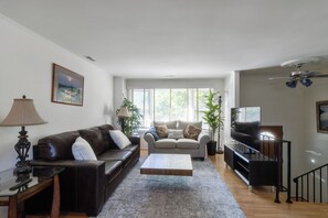 A living room with a dark brown leather sofa, a grey sofa, a coffee table, a TV, and a ceiling fan.