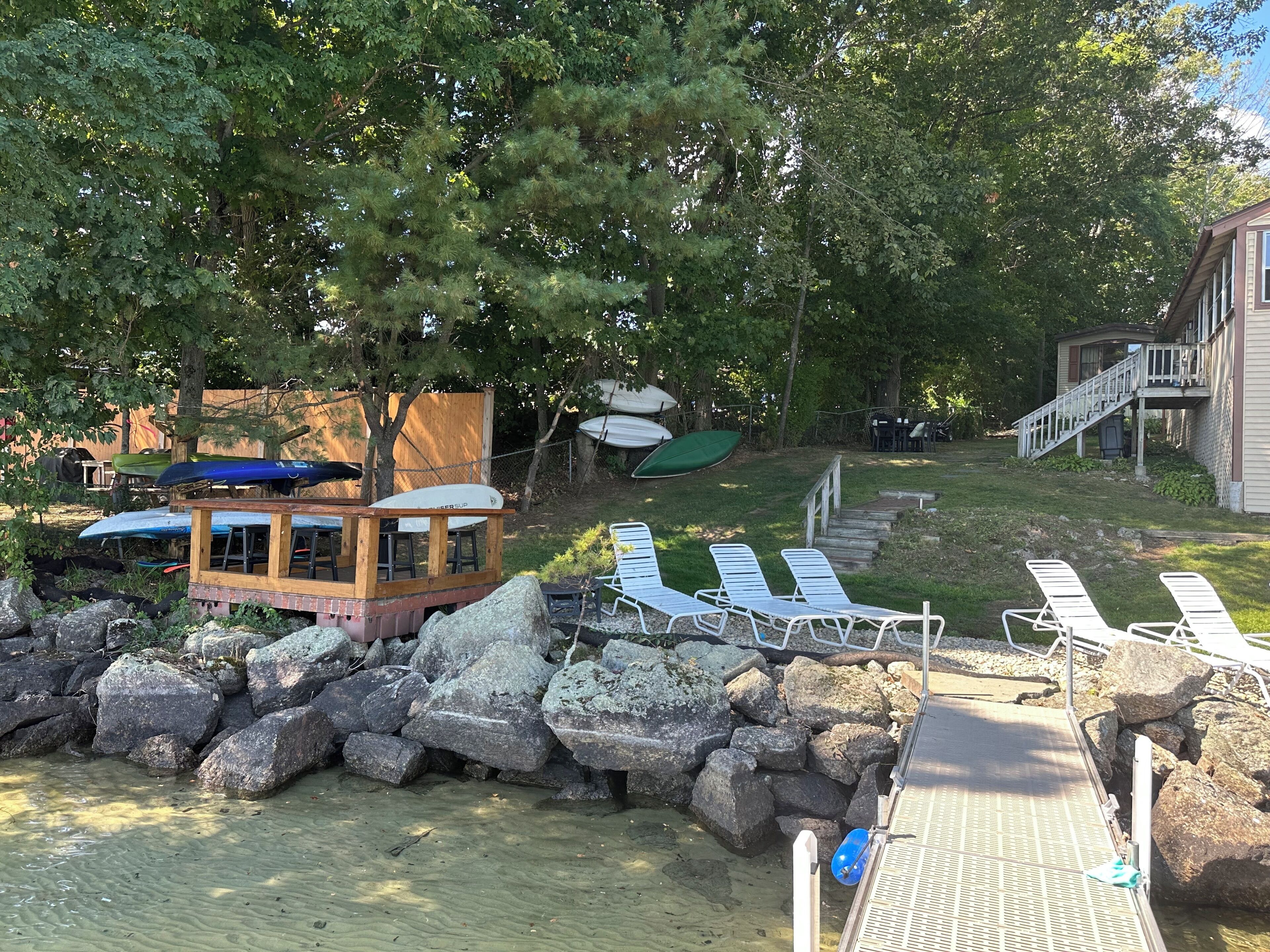 A wooden deck with white lounge chairs, a small wooden structure with a roof, and a stone wall.