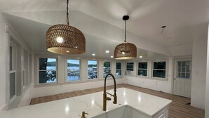 Una cocina amplia con una isla grande, encimeras de mármol blanco y un grifo dorado. Hay dos lámparas colgantes con un diseño tejido.