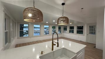 Une cuisine spacieuse dotée d’un grand îlot central, de plans de travail en marbre blanc et d’un robinet doré. Deux suspensions décoratives au design tissé illuminent l’espace.