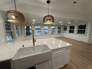 Una cocina amplia con una isla grande, armarios blancos y vistas a un lago a través de amplios ventanales.