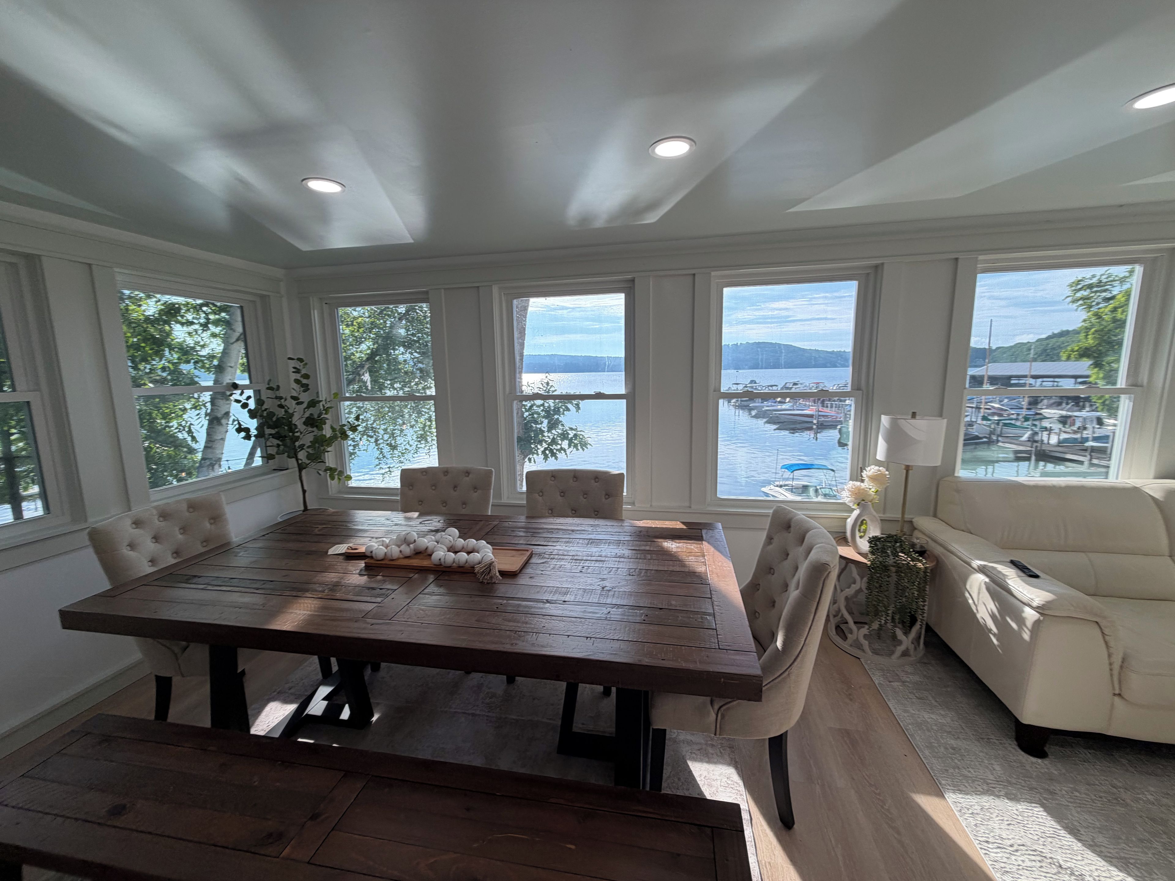 Ein Essbereich mit Holztisch und -stühlen, großen Fenstern mit Blick auf eine Marina und einem Sofa im Vordergrund.