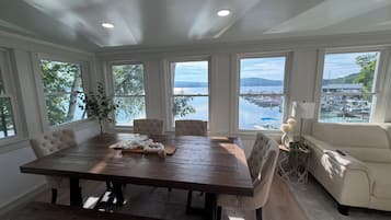Ein Essbereich mit Holztisch und -stühlen, großen Fenstern mit Blick auf eine Marina und einem Sofa im Vordergrund.