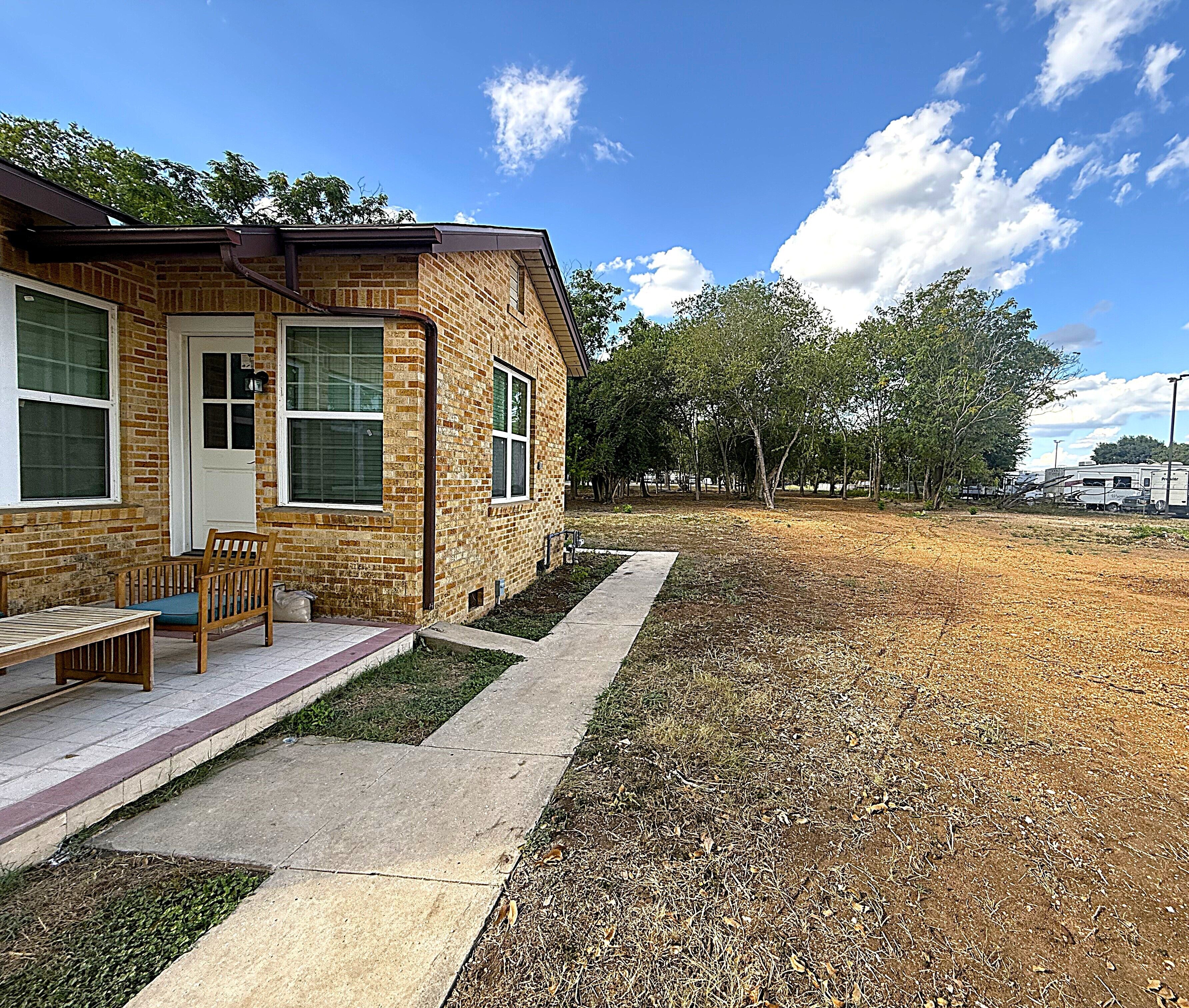 A brick building with a porch, a bench, and a pathway leading to a grassy area.