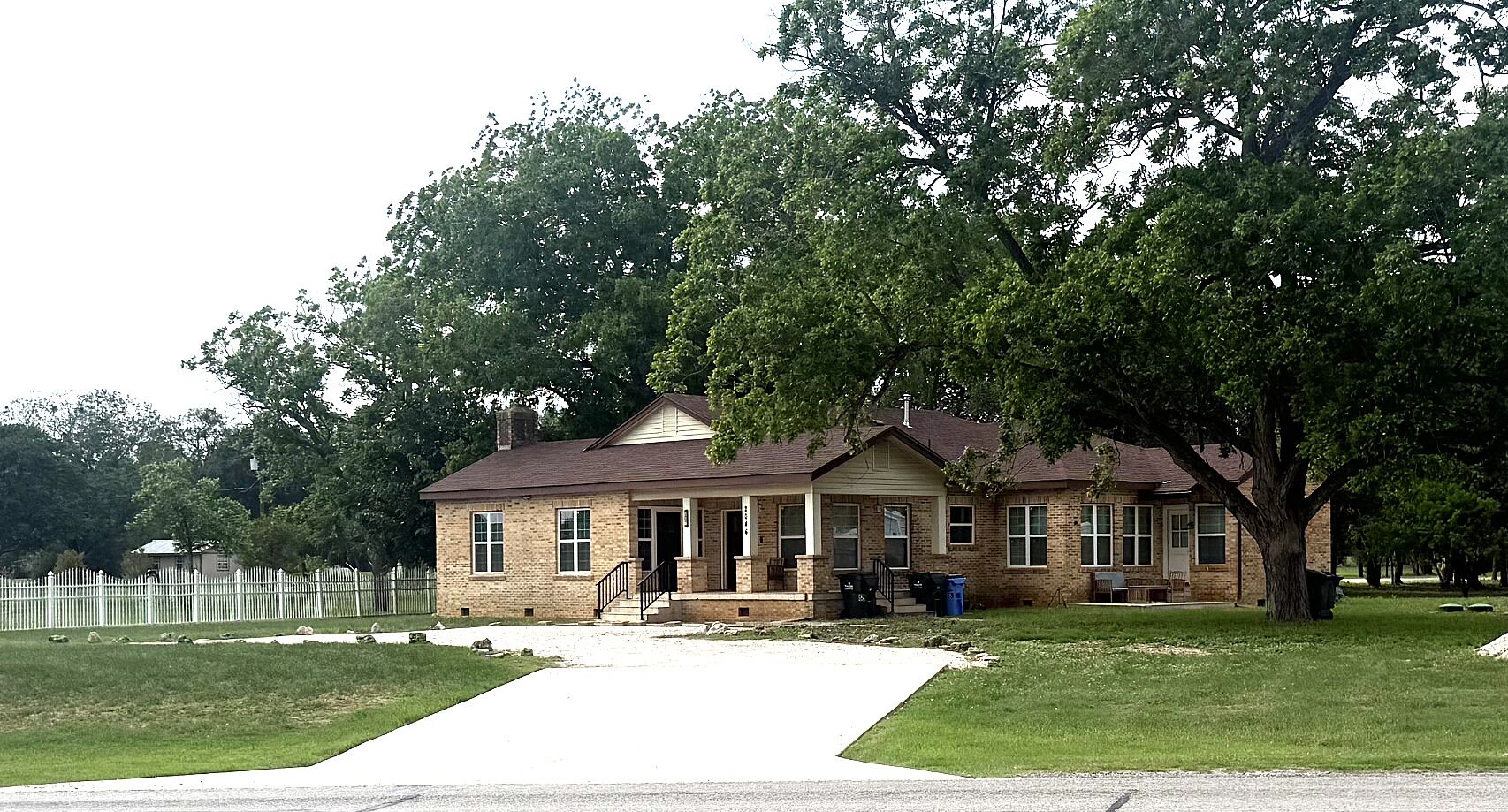 A two-story brick house with a front porch, a small attached garage, and a fenced yard.