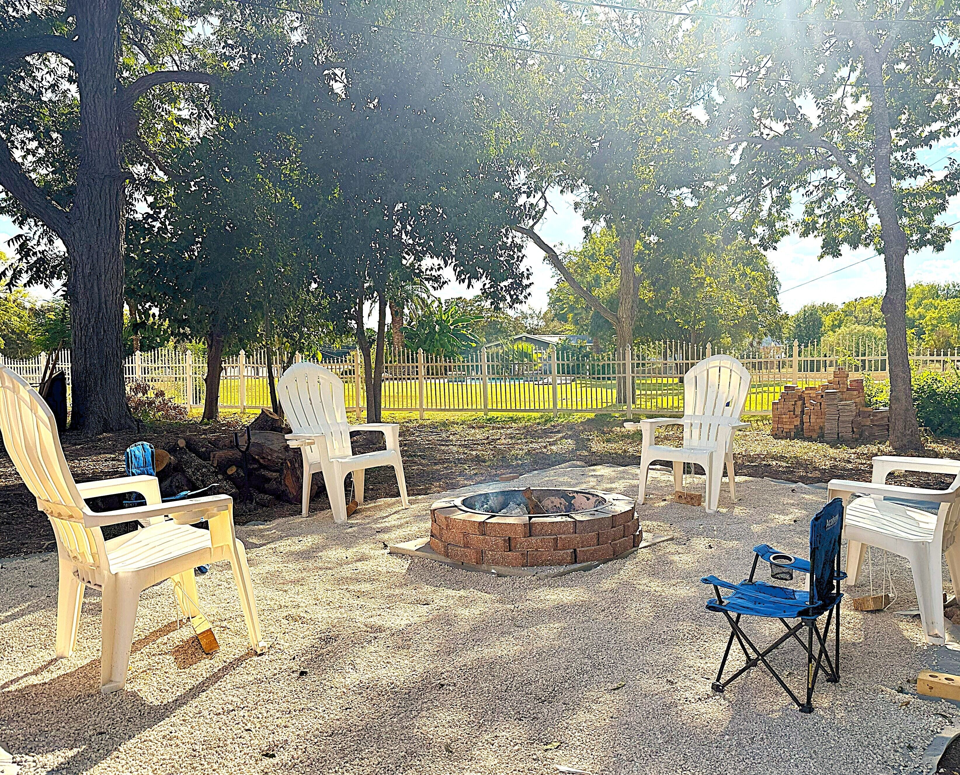 A backyard with a fire pit, white plastic chairs, and a blue folding chair.