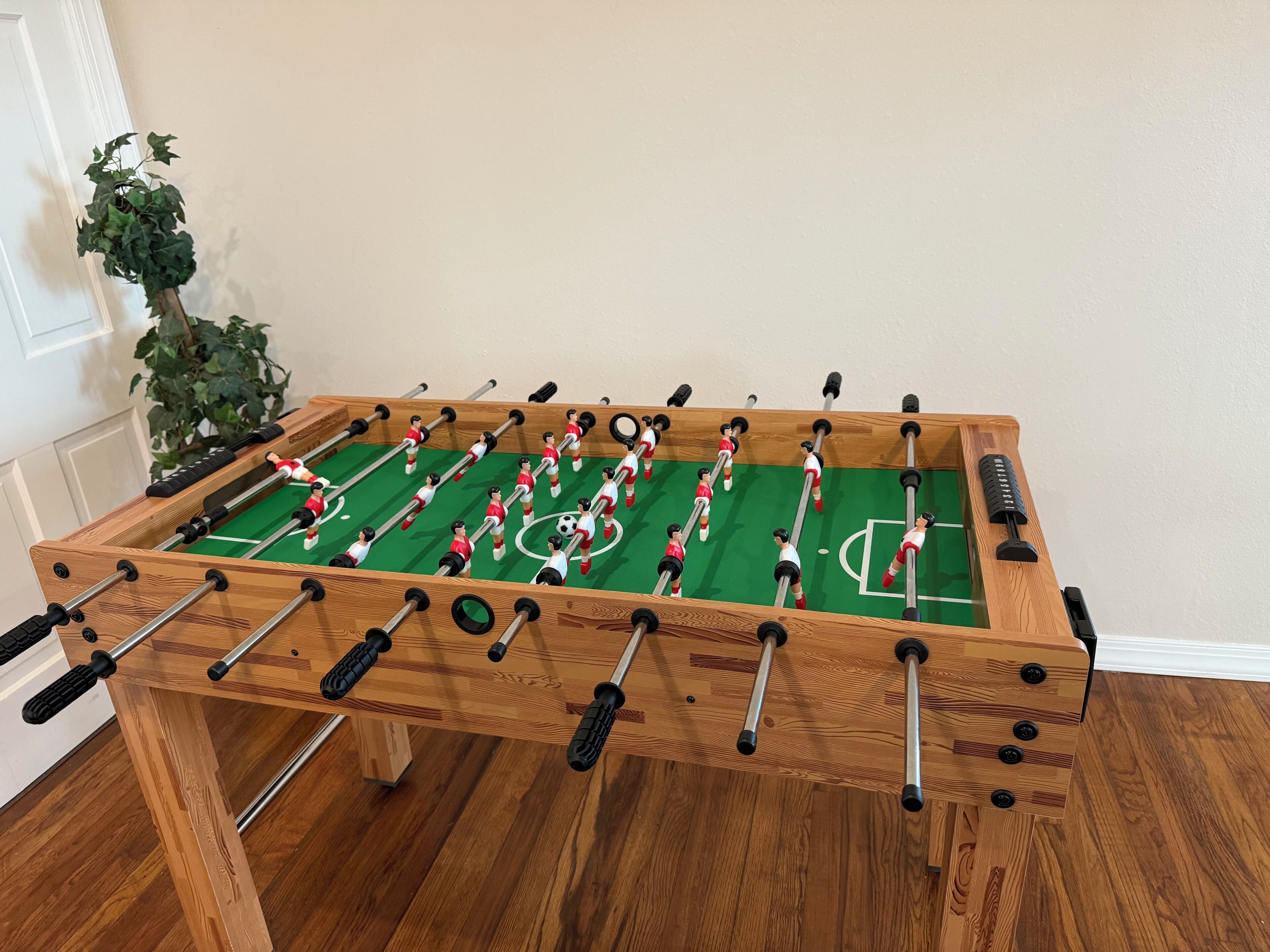 Ett fotbollsspel i trä med en grön spelyta och röda och vita spelfigurer.
