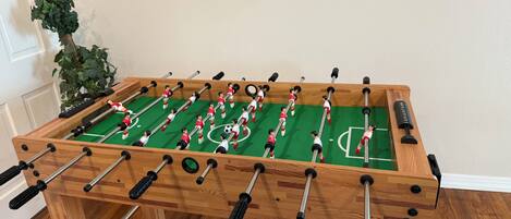 Ett fotbollsspel i trä med en grön spelyta och röda och vita spelfigurer.
