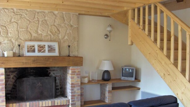 Ein gemütliches Wohnzimmer mit Kamin aus Stein, einer Holztreppe und einem Fernseher auf einem Regal.