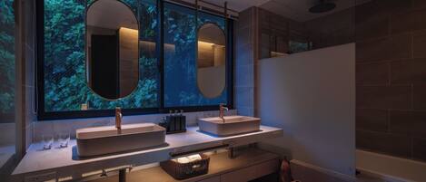 Un baño moderno con dos lavamanos, un espejo grande y un ventanal con vistas a la vegetación.