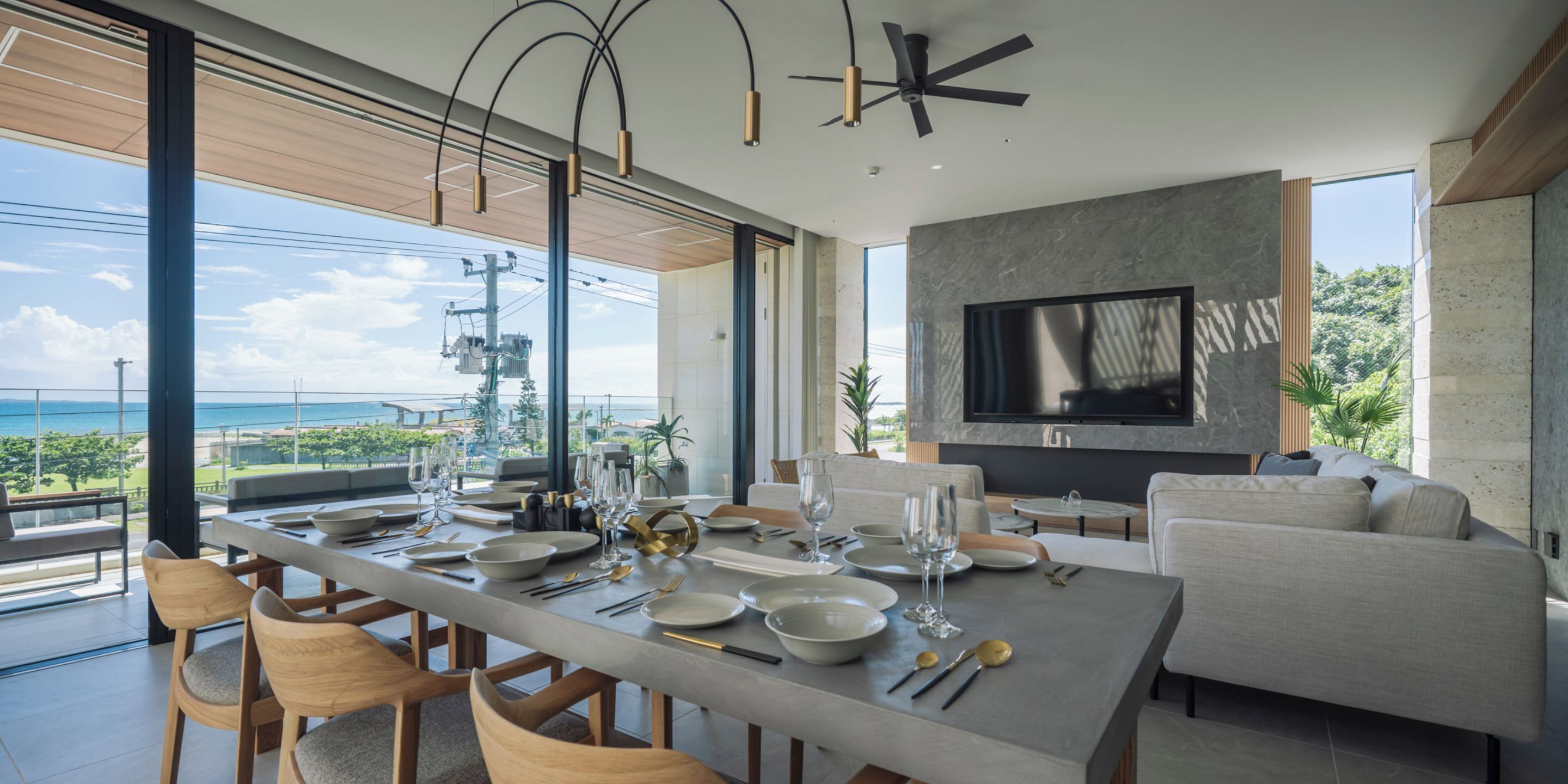 A modern dining area with a large table set for a meal, a sofa, and a TV mounted on the wall.
