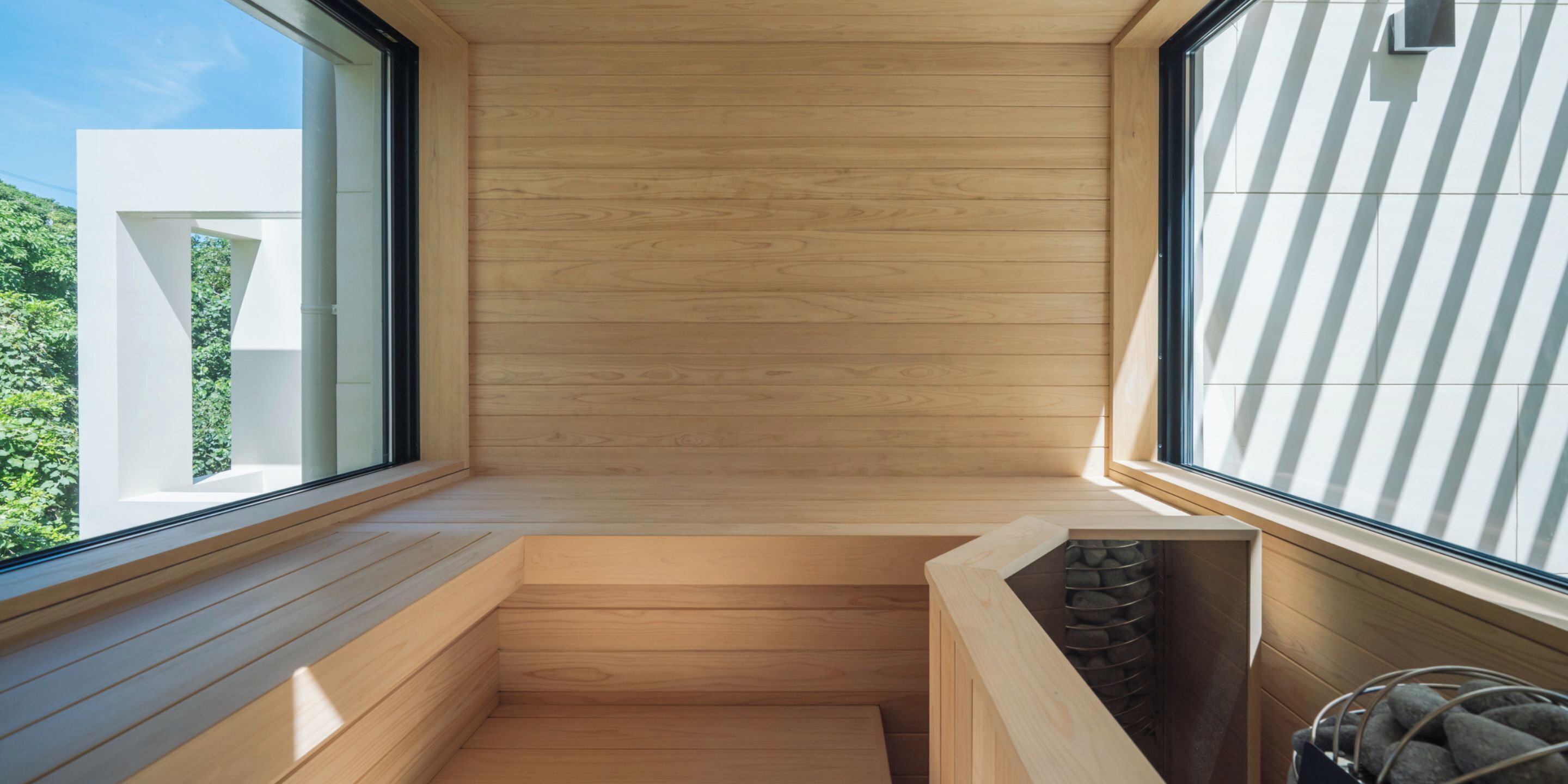 Una sauna con paredes y bancos de madera, ventanas amplias y vistas al verde exterior.