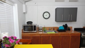 Una cocina con armarios de madera, microondas, tostadora, lavamanos y un reloj en la pared.