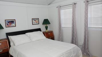 A neatly made bed with white linens, a wooden nightstand with a lamp, and two framed pictures on the wall.