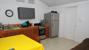 Una cocina compacta con estufa, horno y refrigerador, una mesa de comedor con mantel amarillo y un reloj en la pared.
