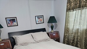 Ein ordentlich bezogenes Bett mit weißer Daunendecke, zwei Nachttische mit Lampen und eine Wand mit gerahmten Bildern.