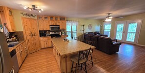 A spacious kitchen with wooden cabinets, a central island, and a dining area with a brown leather couch. - Cozy Cabin Greers Ferry Lake View (Clinton)