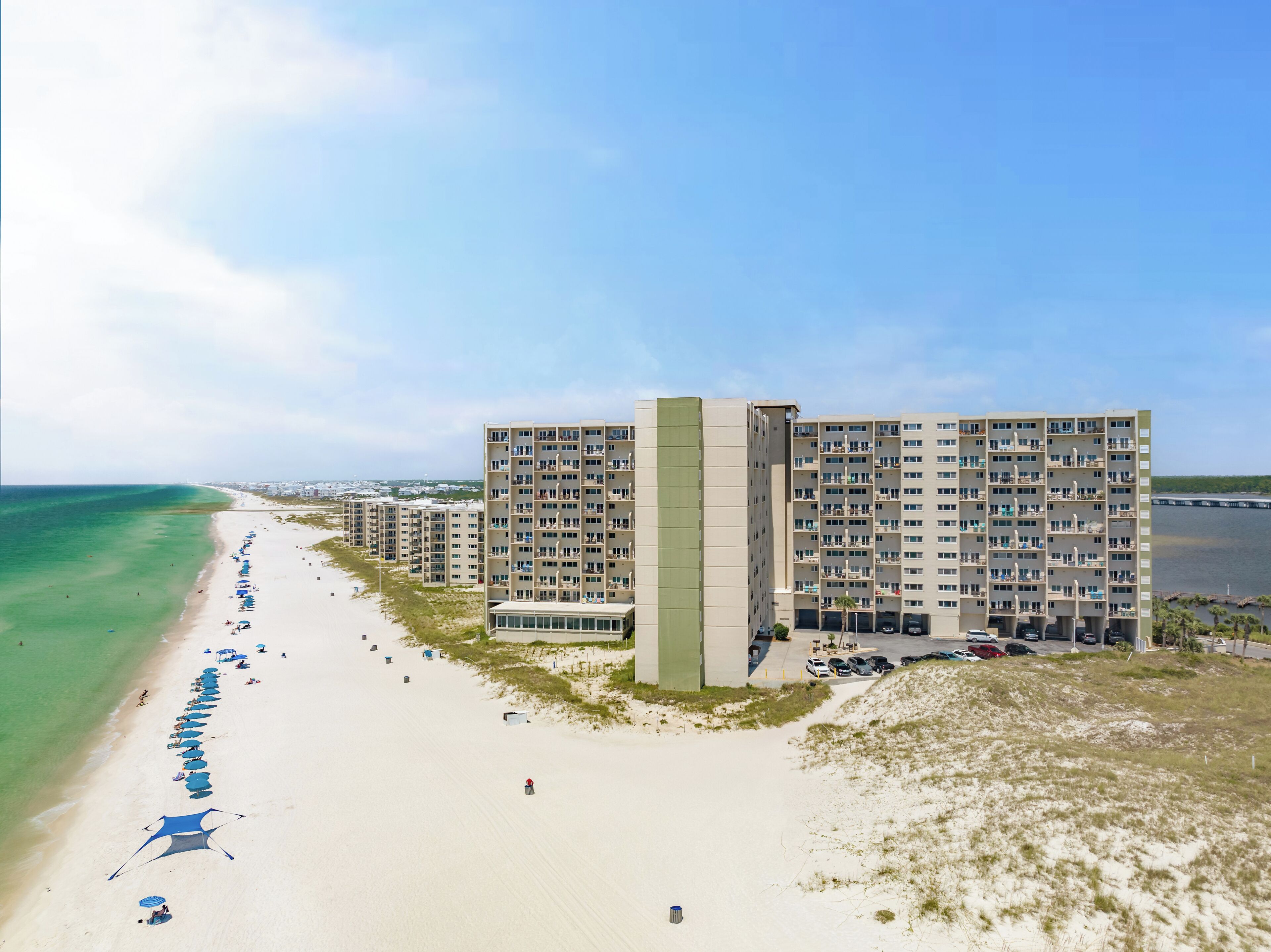 Ein Hotel direkt am Strand mit mehreren Etagen, einem Sandstrand mit Sonnenschirmen und freiem Blick auf den Ozean.