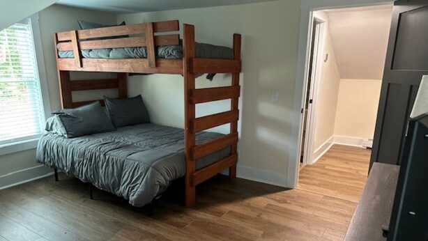 Une chambre avec un lit superposé, un plancher en bois, une porte et un téléviseur.