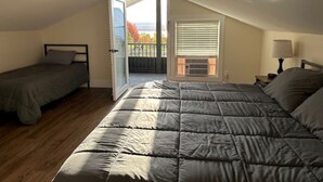 Une chambre avec deux lits, un balcon et une fenêtre avec des stores.