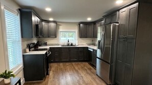 Une cuisine moderne avec des meubles de couleur sombre, des appareils électroménagers en acier inoxydable et un plancher en bois.