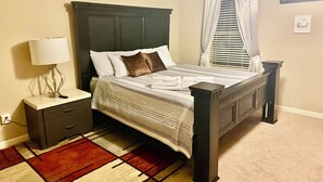 Una cama bien hecha con una colcha a rayas y almohadas, una mesita de noche con una lámpara y una alfombra estampada en rojo y blanco.