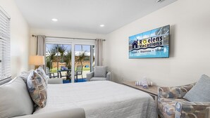 A hotel room with a bed, a sofa, a table, and a TV displaying 'Rosenelens Vacations'. - Unleash Island Bliss - Aloha Kai #34 & #37 - Roelens (Siesta Key)