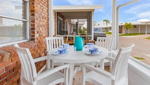 A white table with blue and white patterned plates, a turquoise pitcher, and white chairs in a covered outdoor area with a brick wall and a view of a car and buildings in the background. - Unleash Island Bliss - Aloha Kai #34 & #37 - Roelens (Siesta Key)