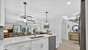 Una cucina moderna con mobili bianchi, elettrodomestici in acciaio inossidabile e illuminazione a sospensione.