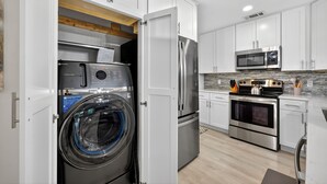 Una cucina moderna con mobili bianchi, elettrodomestici in acciaio inossidabile e lavatrice asciugatrice integrate.