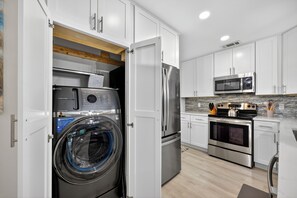 A modern kitchen with white cabinets, stainless steel appliances, and a built-in washer and dryer.