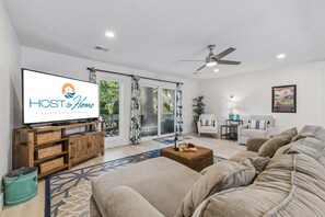 A modern living room with a flat-screen TV, a wooden entertainment unit, a sofa, a coffee table, and a ceiling fan.