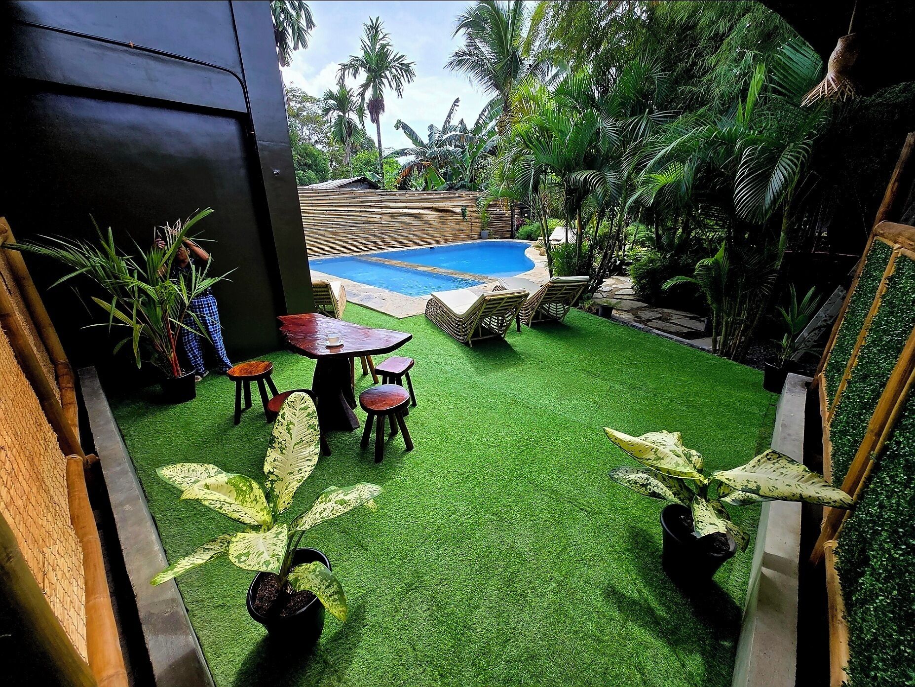 Un jardin avec une piscine, du gazon synthétique et des plantes en pot.