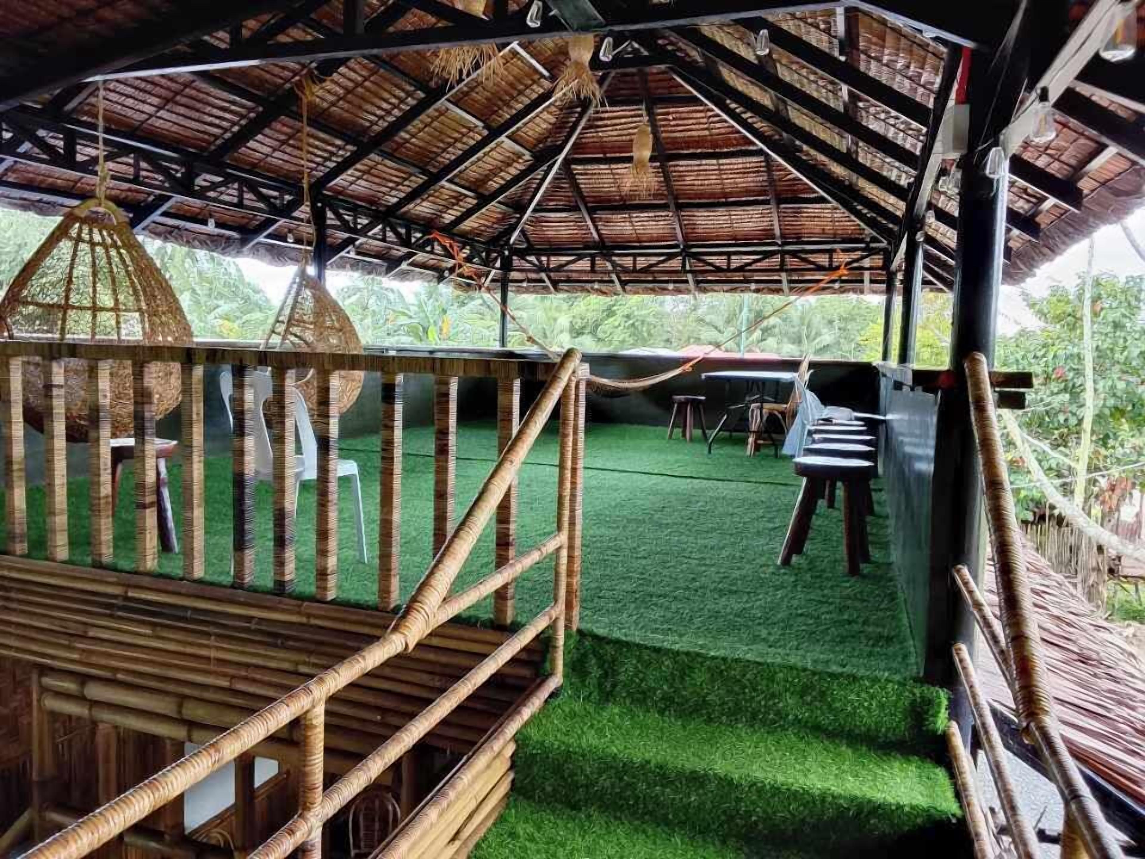 A covered outdoor area with a thatched roof, green artificial grass, and wooden furniture.