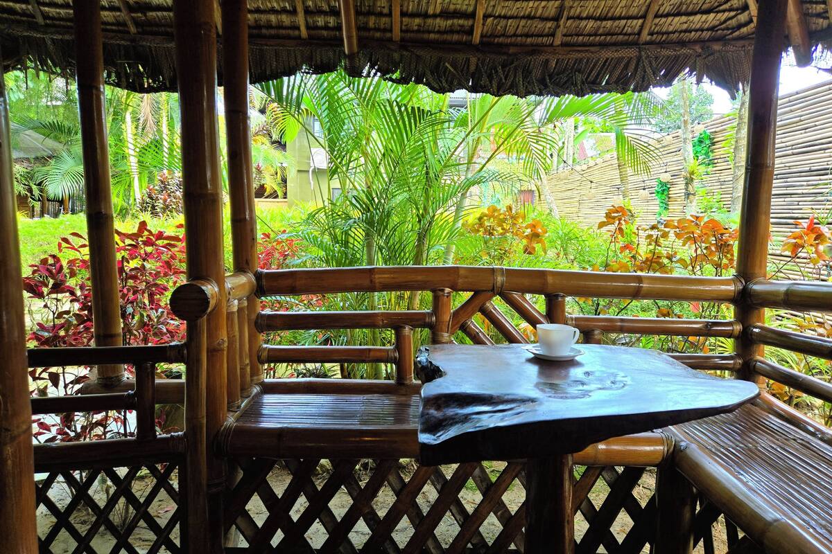 Un espace extérieur aménagé avec des meubles en bambou et une table, entouré d’une végétation luxuriante et de plantes tropicales.
