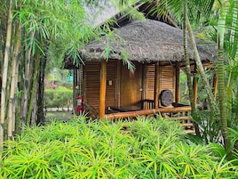A bamboo hut with a thatched roof, surrounded by lush greenery.